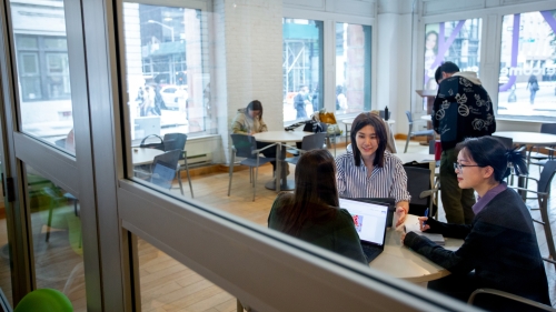 Students sit at tables with computers