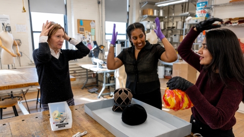 Three people in a workshop discussing hats.