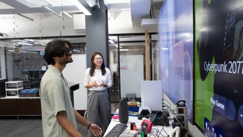 Two students smiling as they look at a wall-mounted screen.